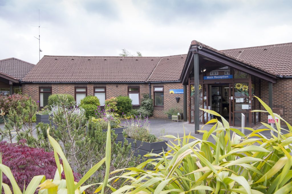 Photo of the Hospice entrance on a sunny day with greenery in the foreground.