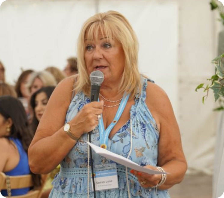 Photograph of a lady in a blue sun dress speaking into a microphone