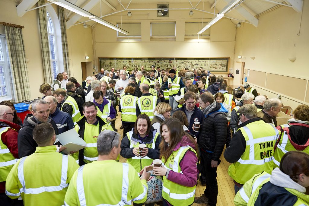 A big room full of people from the tree collection event wearing high vis jackets and talking amongst themselves