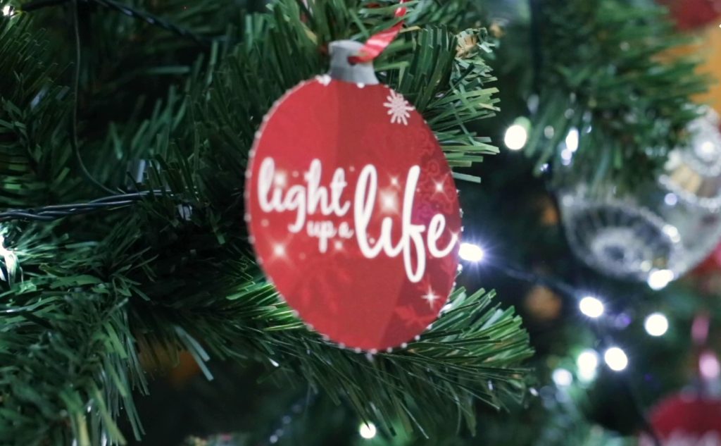 A Christmas tree with a red paper bauble with ;Light up a Life' written on it