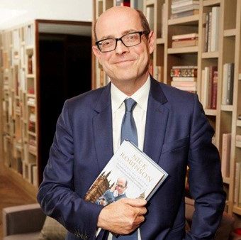 A man in a suite is smiling and holding his own book named Nick Robinson