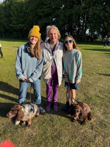 Photo of three Starlight Walk participants with two dogs smiling at the camera while stood in a field in front of some trees