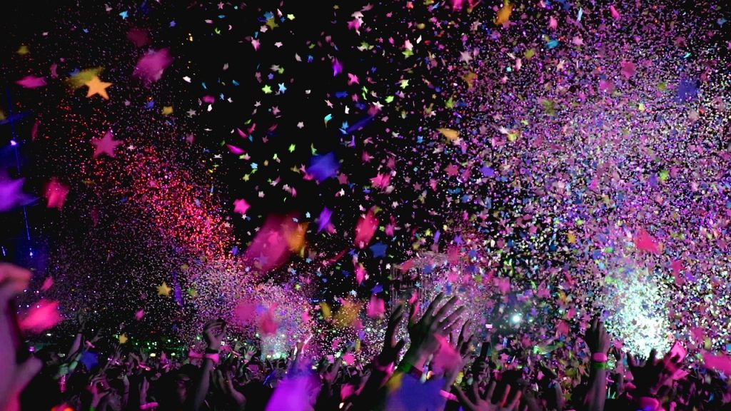 Photo of a party scene with colourful confetti against a dark background with people's hands reaching up