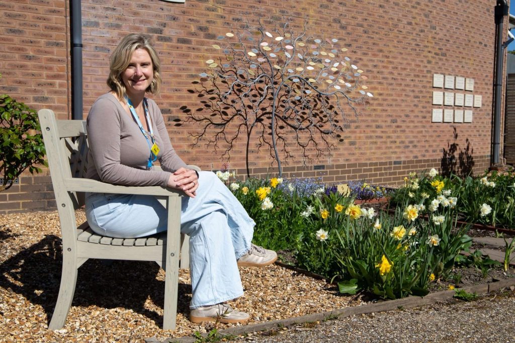 Amy Williams sat on a bench next to the Hospice Memory Tree, looking at the camera.