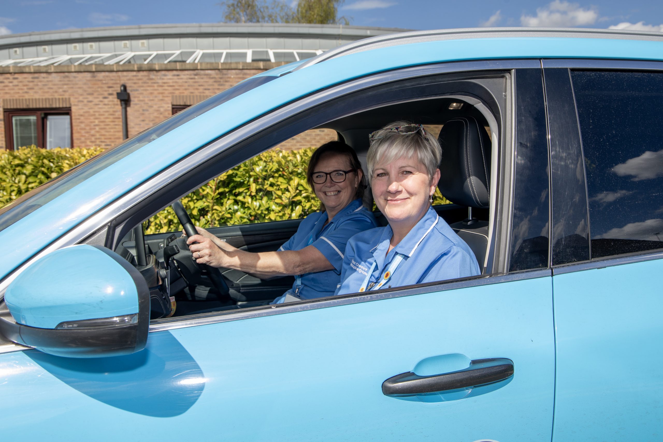 Photo through the passenger side window of a Hospice @Home car of two smiling nurses ready to drive away