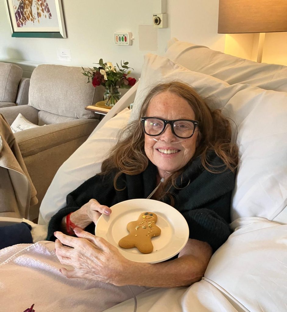 Photo of a patient in a Hospice bed smiling happily and holding a plate with a gingerbread man on it.