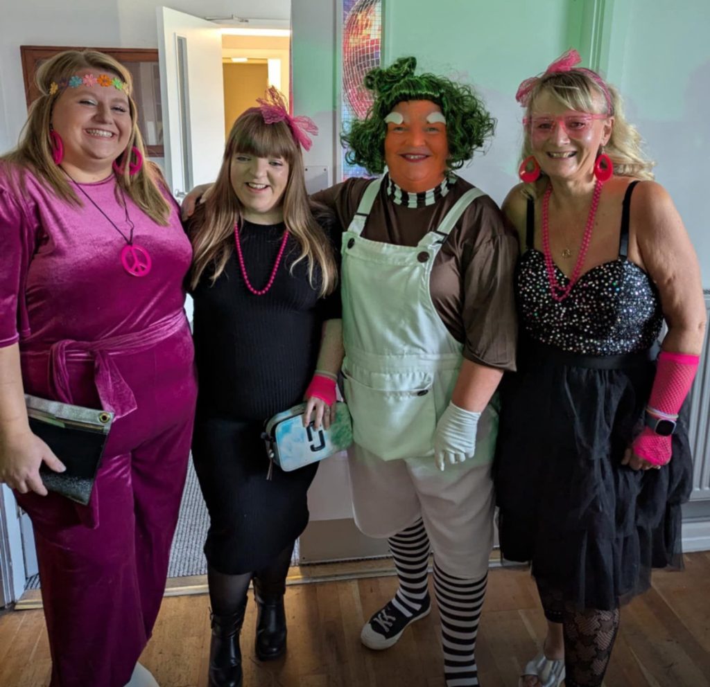 Group of four people dressed us in 70/80's outfits looking at the camera.