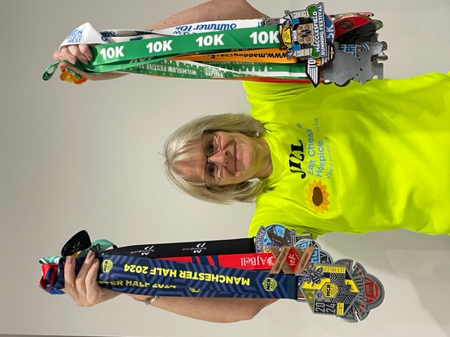Jill Booth holding up lots of medals facing the camera, wearing a bright yellow Hospice t-shirt.