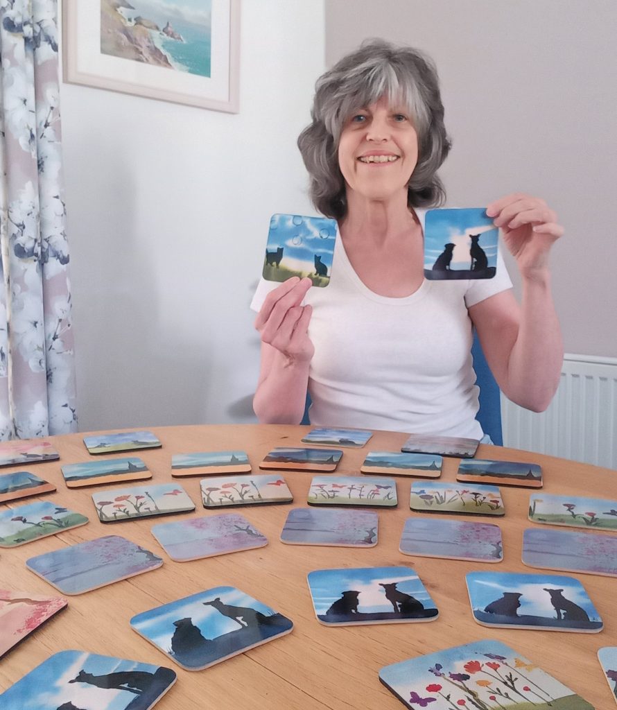 Sheila King holding up two coasters smiling at the camera