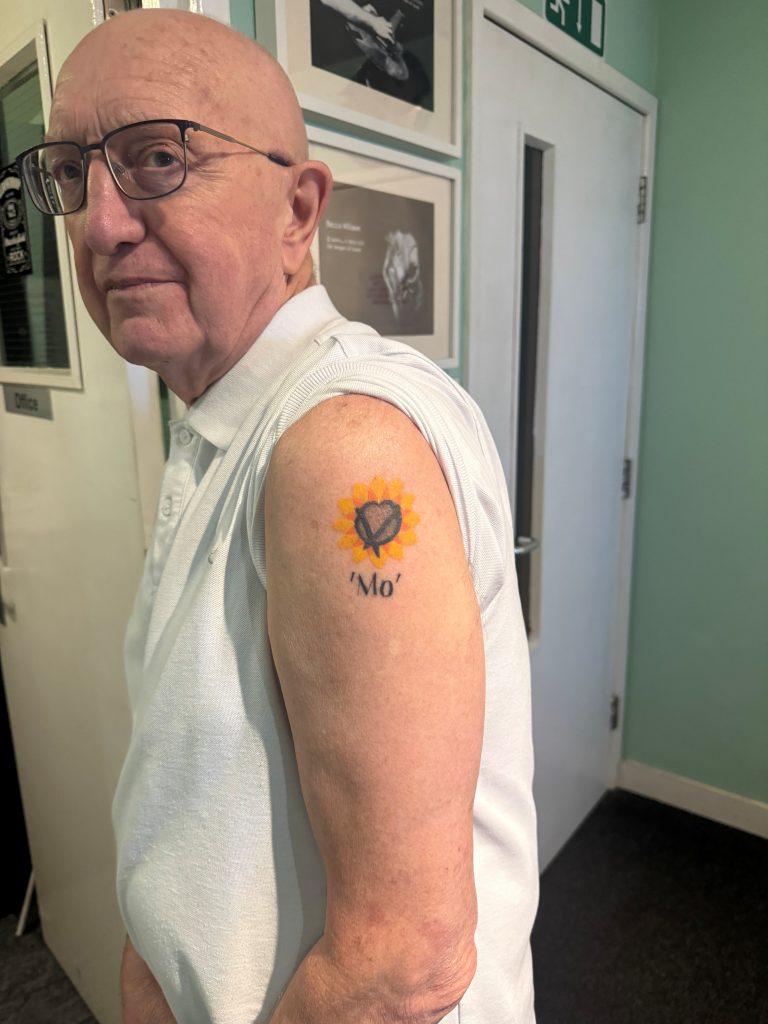 Alan Bailey stood side on with sleeve of his t-shirt rolled up showing his tattoo on shoulder