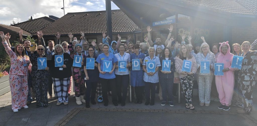 Photo of a large group of East Cheshire Hospice staff outside cheering and holding letters spelling 'you've done it!'.