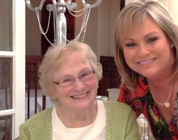 Photo of a an elderly mother and her daughter together dressed up for a special occasion and smiling at the camera