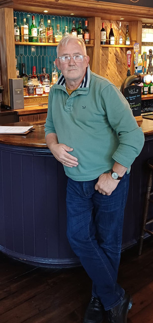 Photo of a man in a light green fleece stood against a bar looking at the camera