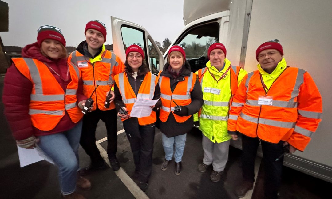 Photo of six people stood next to a white van wearing orange and yellow hi-vis clothing on a winter's day