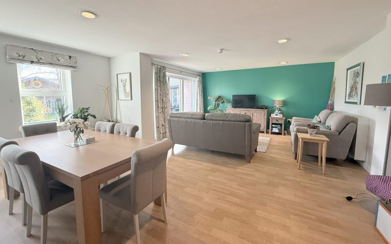 A photo looking into a modern living room with a table, chairs, flowers, sofas and television