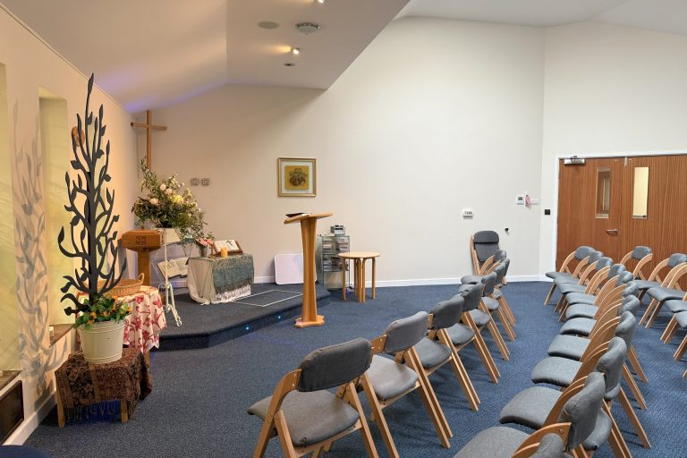 A photo of East Cheshire Hospice's chapel. Chairs are laid out in two lines with a podium at the front of the room.