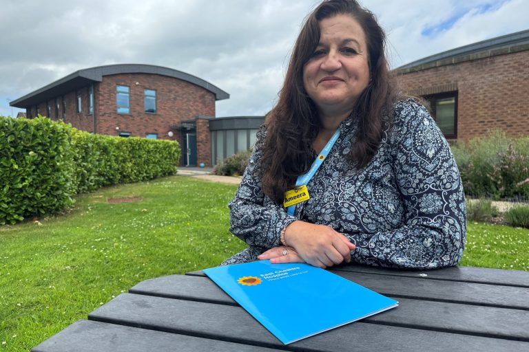 Photo of Community Volunteer Services Lead Ameera Fletcher sitting at a table in the Hospice garden smiling at the camera.