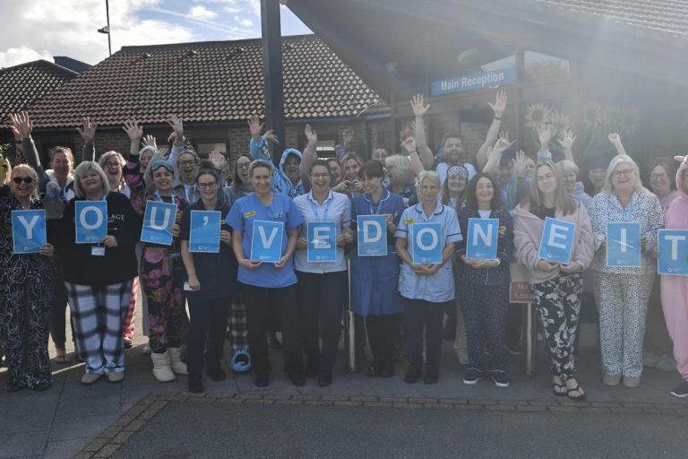 Photo of a large group of East Cheshire Hospice staff outside cheering and holding letters spelling 'you've done it!'.