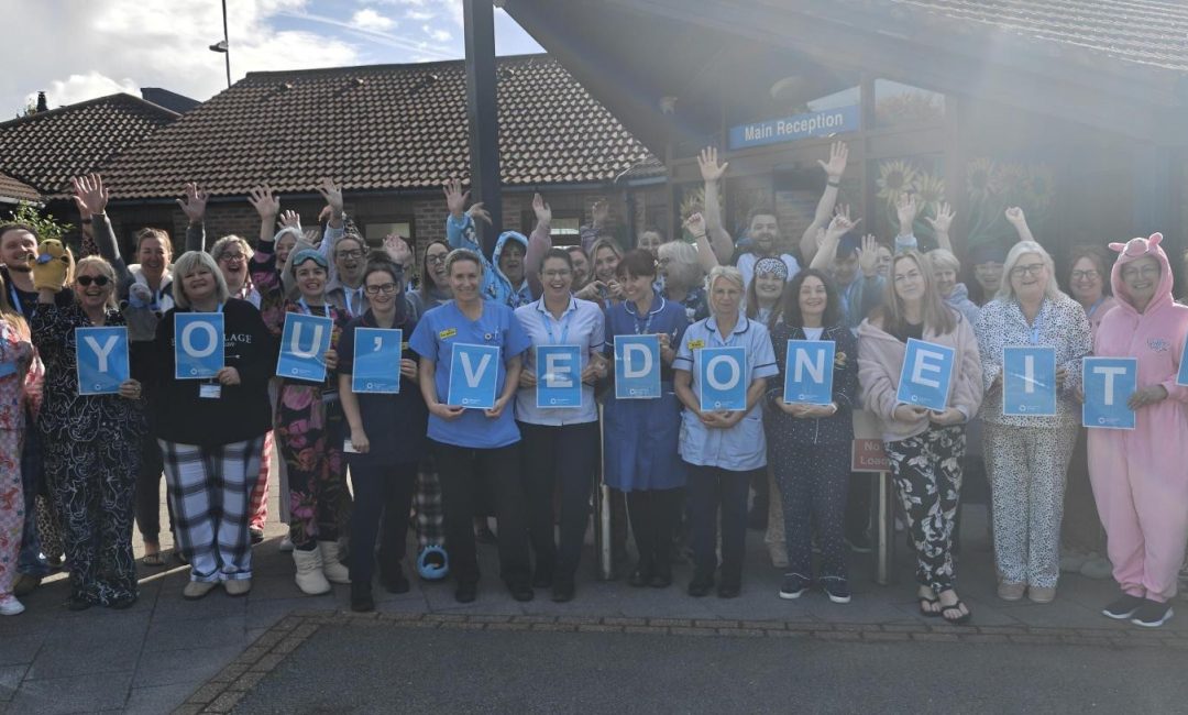 Photo of a large group of East Cheshire Hospice staff outside cheering and holding letters spelling 'you've done it!'.