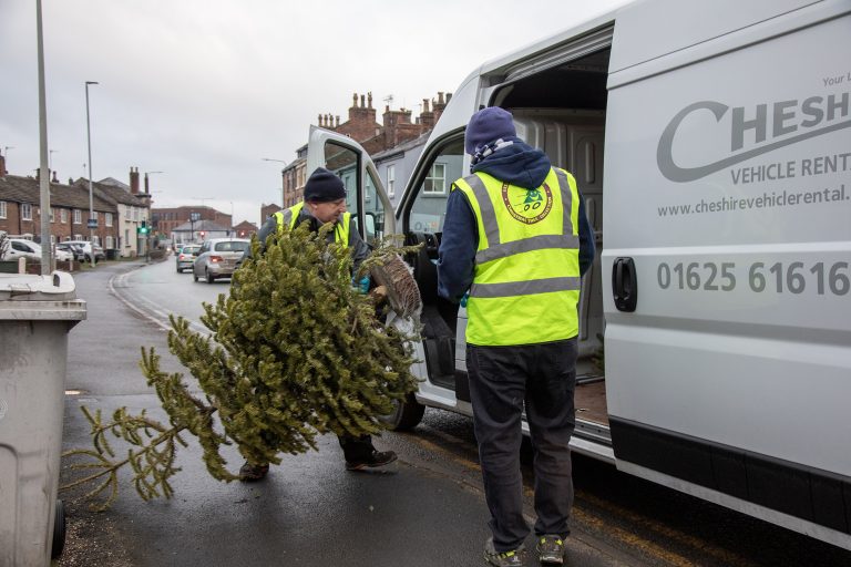 Photo of two volunteers in hi-vis loading a Christmas tree into the side of a large van.
