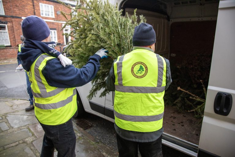 Two people wearing high vis jackets carrying a Christmas tree from the tree collection fundraising event