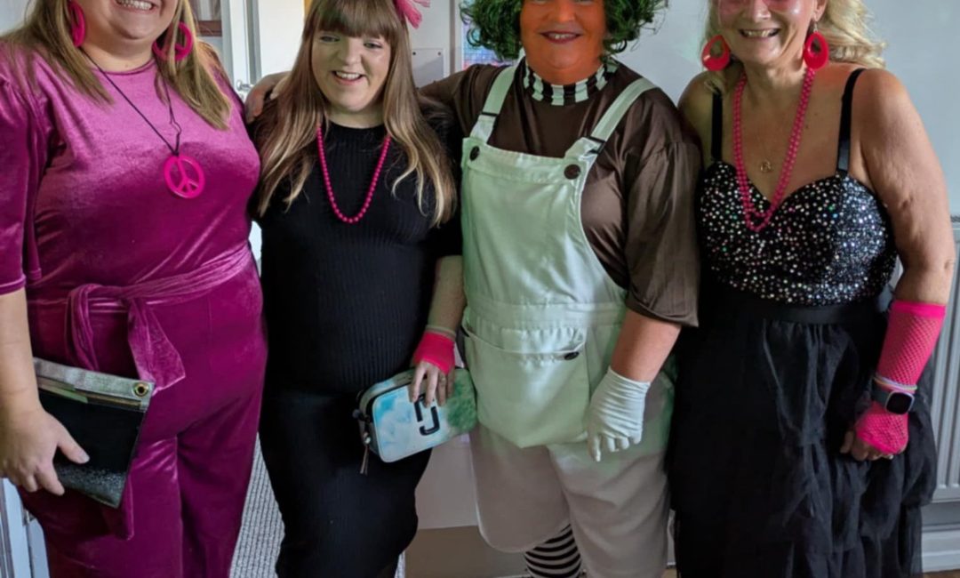 Group of four people dressed us in 70/80's outfits looking at the camera.