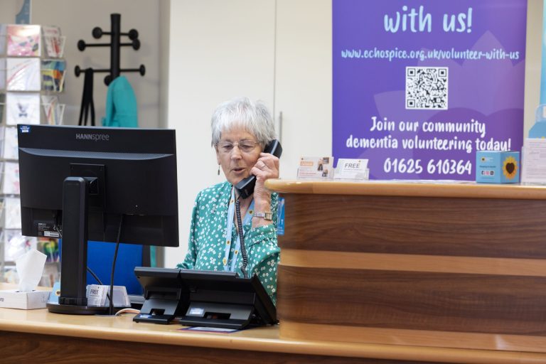 Photo of a Hospice volunteer receptionist using the telephone behind the reception desk.
