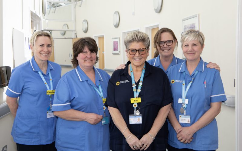 Photo of 5 clinical staff stood in a naturally lit corridor smiling at the camera
