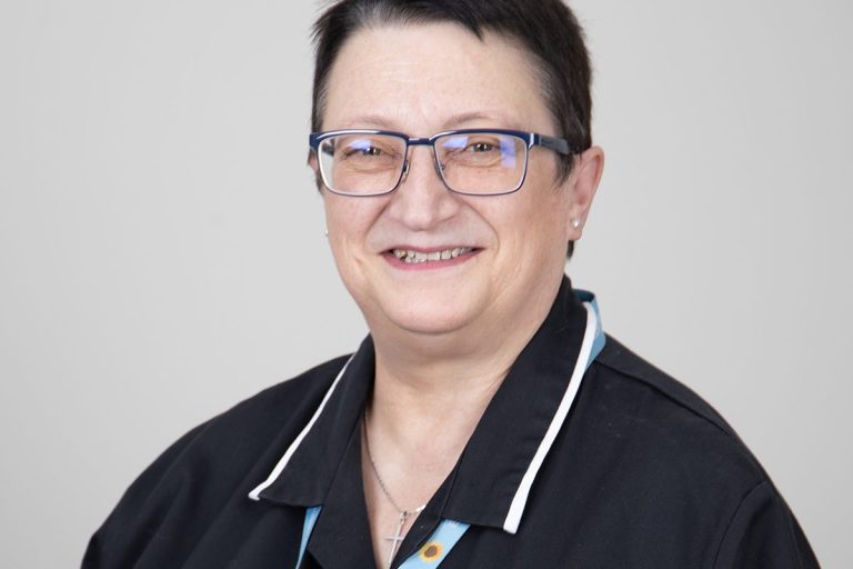 Hospice chaplain Marion smiling at the camera in front of a grey background