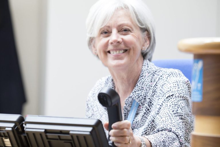 Lady sat her desk smiling at the camera about to pick up the phone