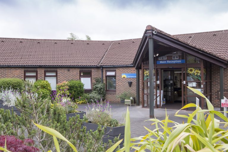 Photo of the front of the Hospice with greenery and plants in the foreground