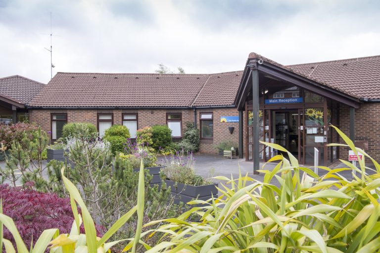 Photo of the Hospice entrance on a sunny day with greenery in the foreground.