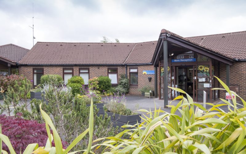 Photo of the Hospice entrance on a sunny day with greenery in the foreground.