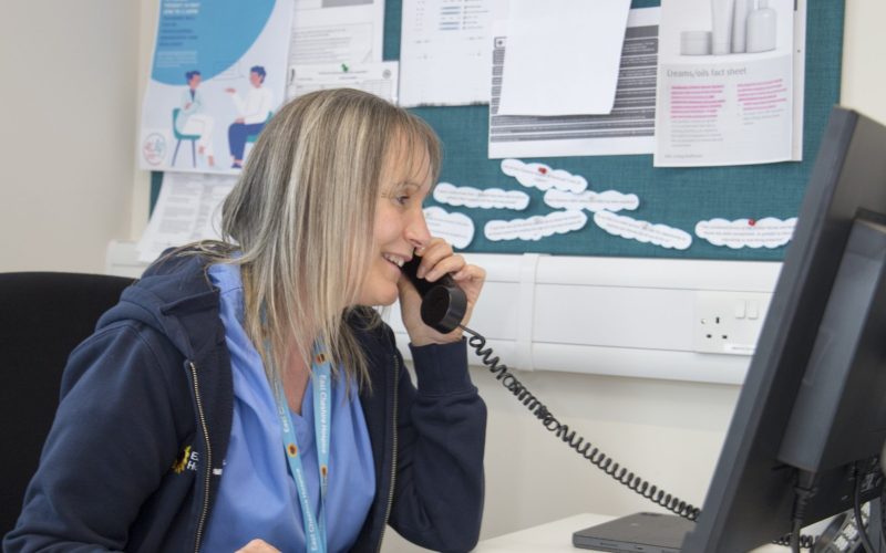 Hospice @Home staff member in blue uniform on the phone in an office in front of a computer