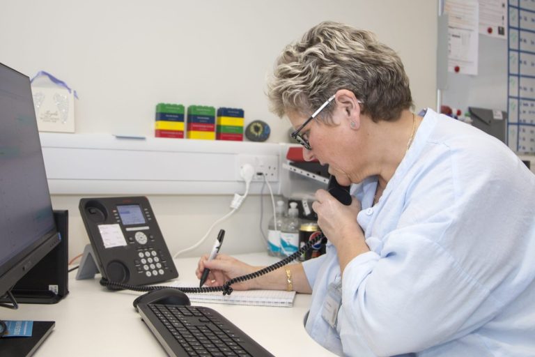 Person sat at a desk on the phone and writing information down