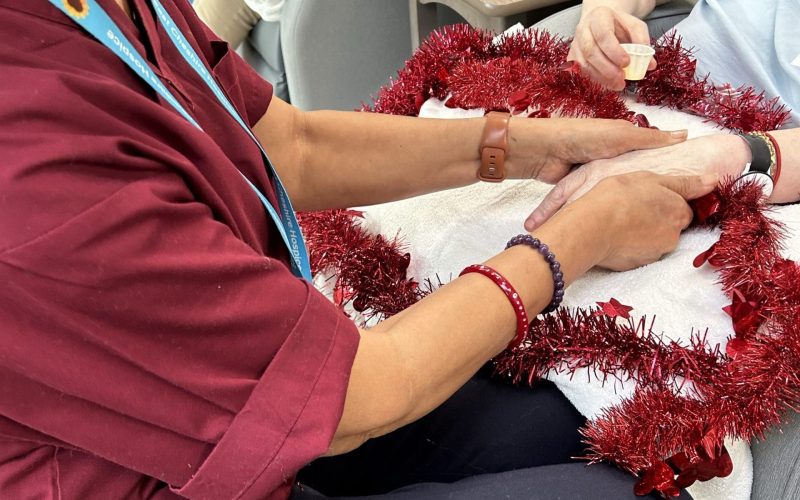 A nurse working in the Hospice caring for a patient and holding her hand. A strip of red tinsel is lying on top of the patient