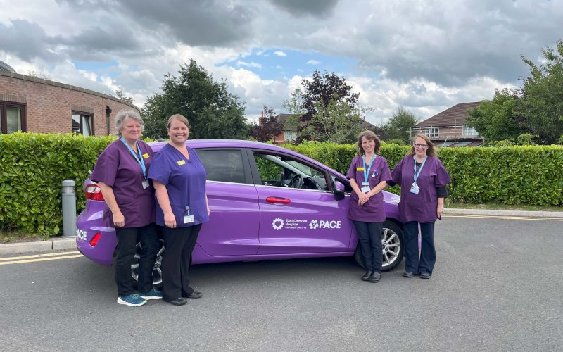 Photo of four PACE staff stood next to a purple PACE branded car.