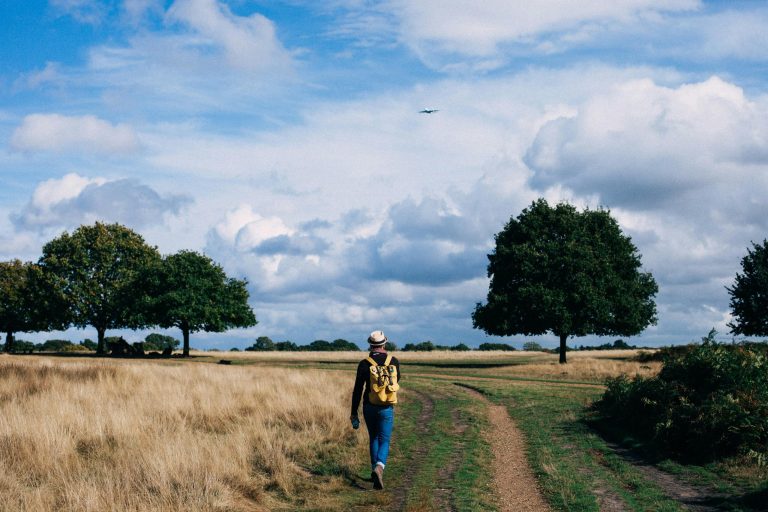 Person walking in a field with a backpack and yellow hat on.