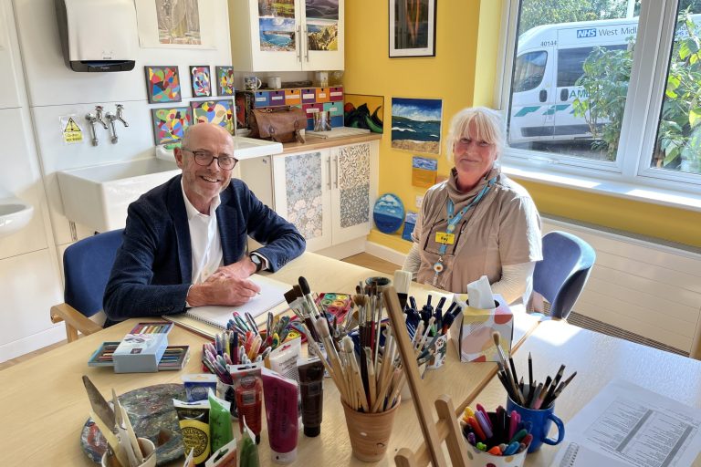 Nick Robinson and Fay Mitchell are sitting at a table ready to paint. The table is full of paintbrushes, paints, colouring pencils and felt tips