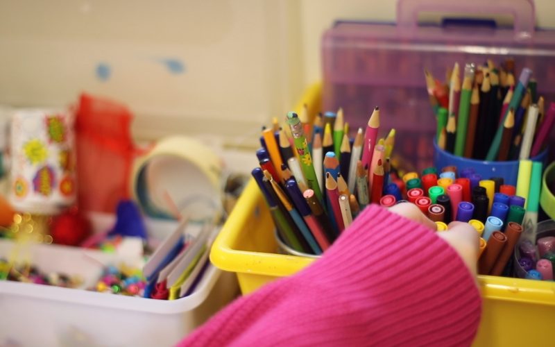 A photo of a hand reaching in to lots of pots of coloured pencils and felt tips
