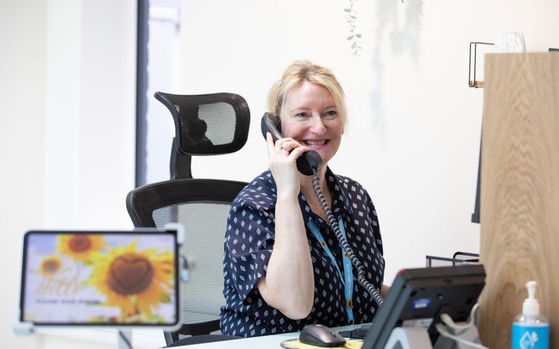 A clinical coordinator sat at a desk on the phone smiling at the camera