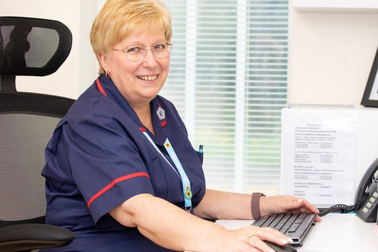 A nurse who works at the Hospice sitting at her desk smiling at the camera