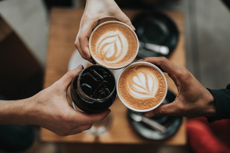 Photo of three people's hands holding coffee cups together