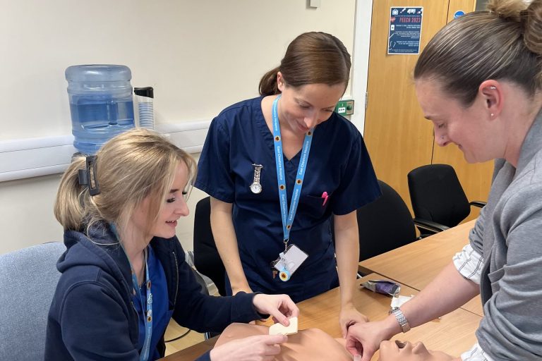 Three ladies practicing medical exercises on a dummy
