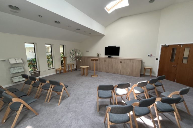 Photo of the Hospice chapel - a large light room with chairs arranged in rows facing a lectern.